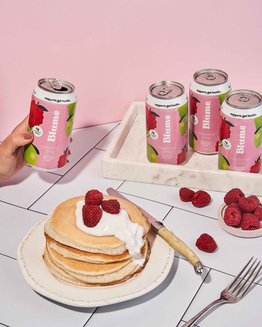 a pancake stack with fresh raspberries and yoghurt on top of it with kombucha in the background