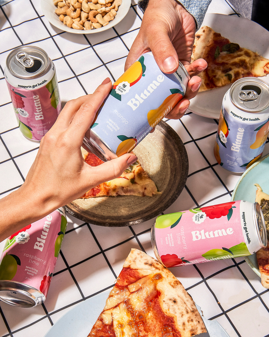 one hand passing a drink to another person's hand with pizzas visible on the table