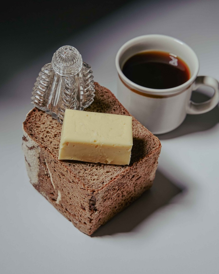Rustic slice of bread topped with butter, paired with a cup of coffee in moody lighting