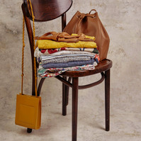 Folded clothes, leather bag and yellow purse styled on vintage wooden chair — Melbourne product and lifestyle flatlay