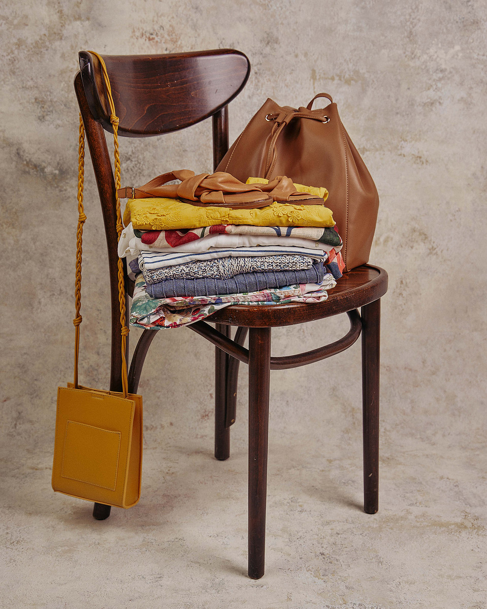 Folded clothes, leather bag and yellow purse styled on vintage wooden chair — Melbourne product and lifestyle flatlay