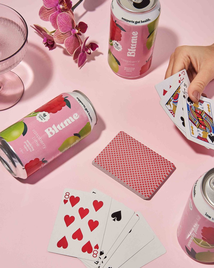 two kombucha cans lying on a pink backdrop with cards 