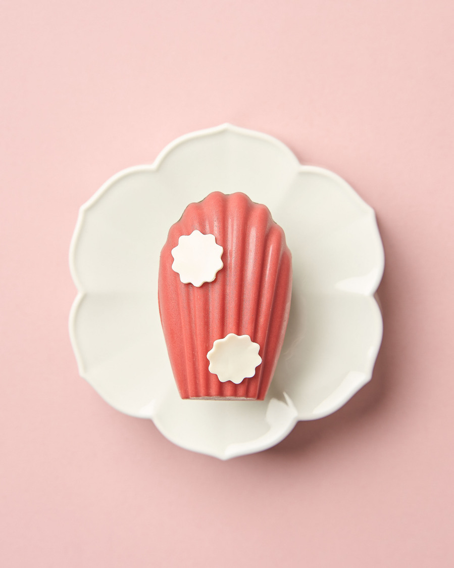 Elegant pink dessert with white flower accents on a white scalloped plate and pastel pink background
