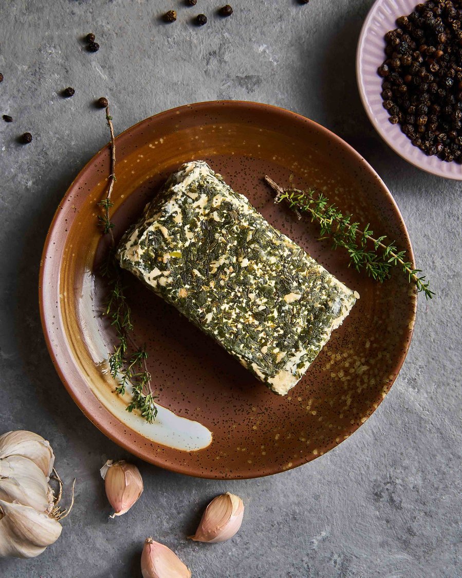 Block of compound butter garnished with herbs and garlic on a rustic ceramic plate