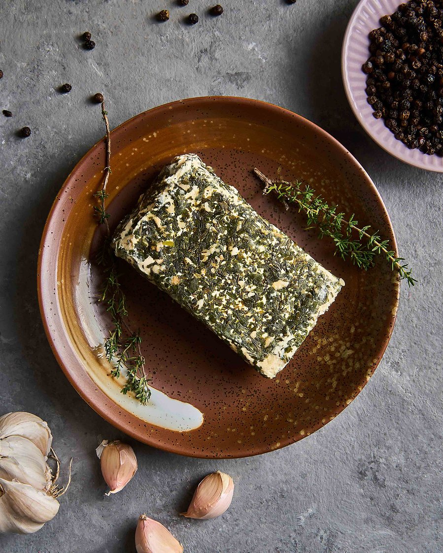 Block of compound butter garnished with herbs and garlic on a rustic ceramic plate