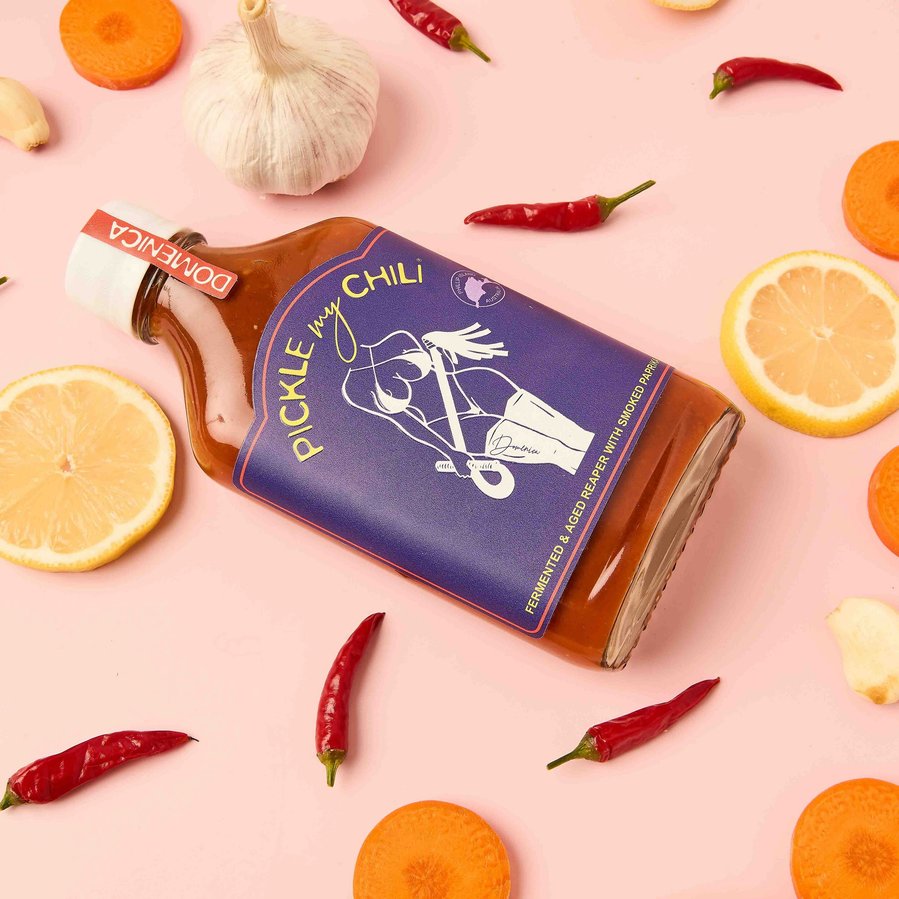chilli sauce surrounded by fresh chilli and lime and garlic on a pink background