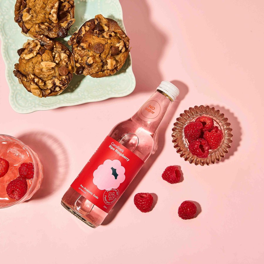 pink kombucha with muffins and raspberries lying next to it