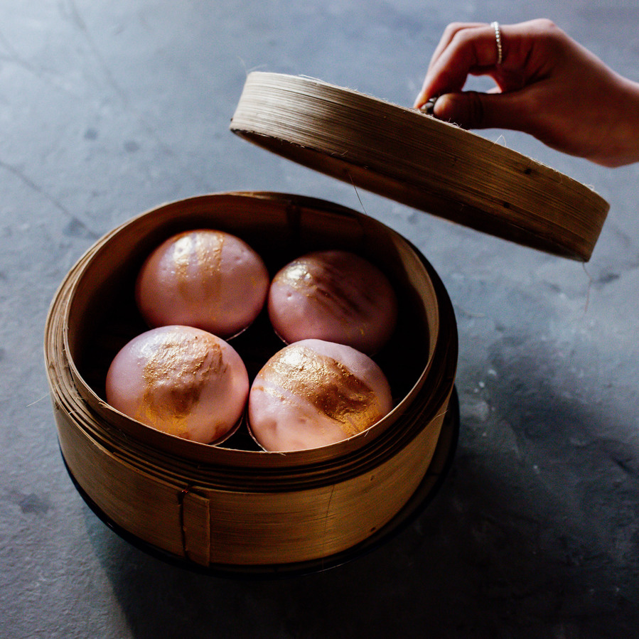 someone's hand opening a basket with pink dumplings in it 
