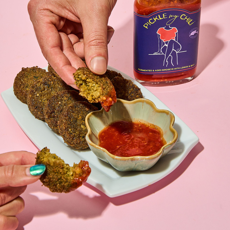 two hands dipping falafels in sauce 