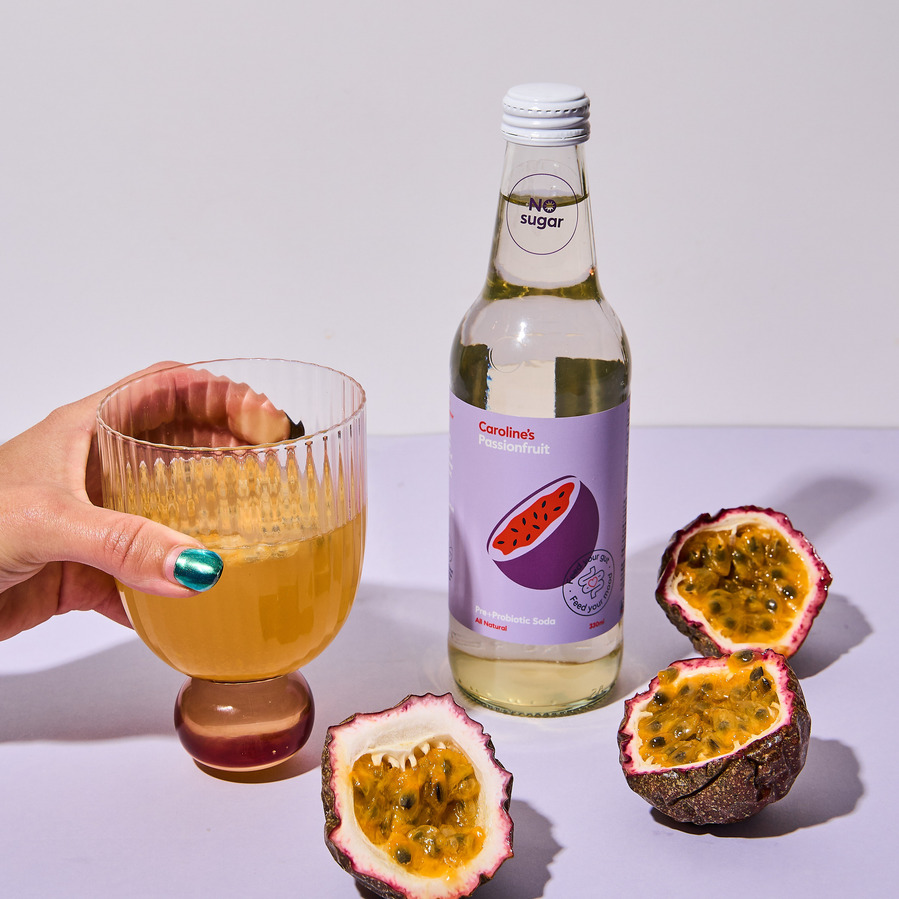 a hand holding a drink, passionfruit and a kombucha next to it