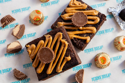 two pieces of brownie decorated with peanut butter with chocolate candies lying around 