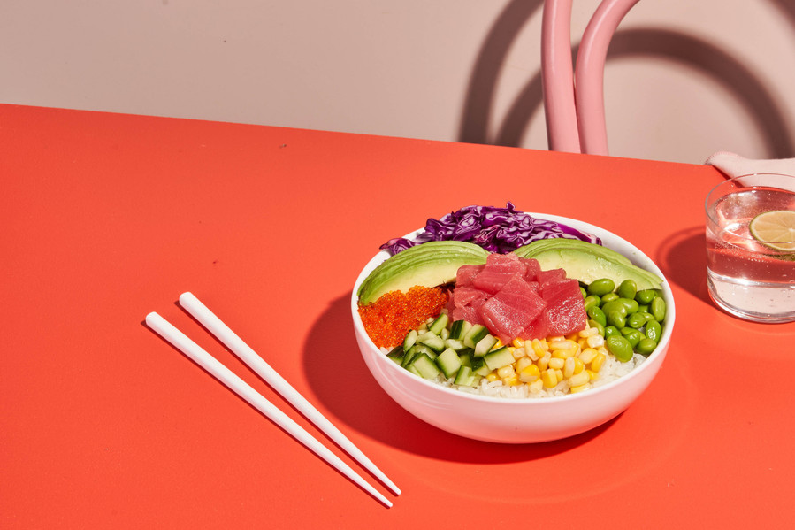 a poke bowl with chopsticks lying on a red surface