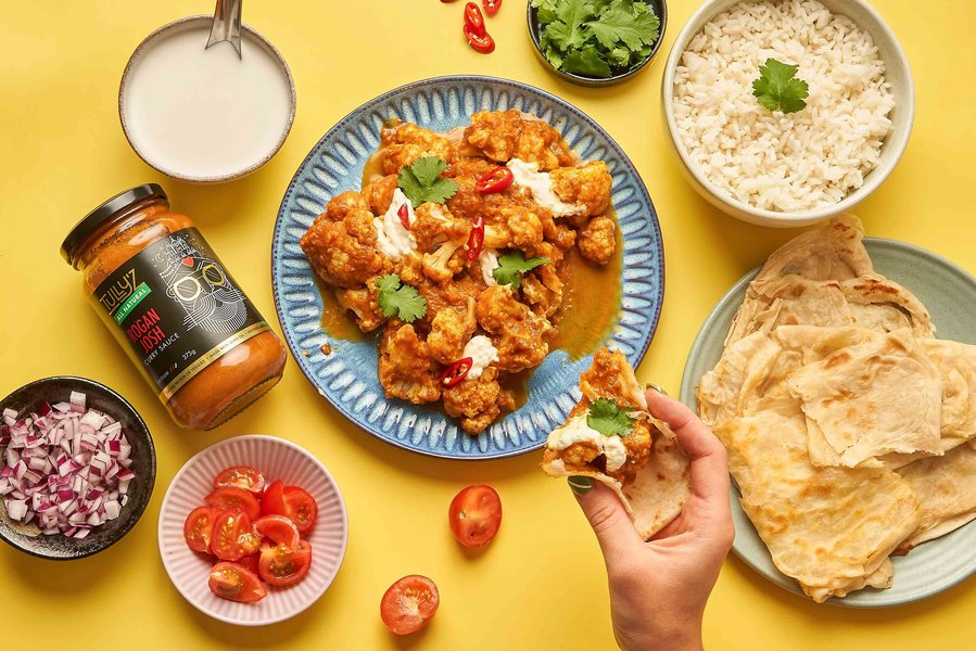 a colourful spread of Indian curry dinner with a hand dipping naan bread in a curry