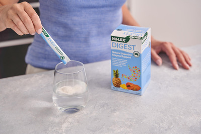 a hand putting a supplement powder into a glass of water