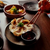 Chopsticks picking up dumplings at a restaurant table with side dishes — Melbourne food photography
