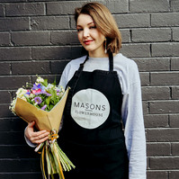 Florist wearing apron holding bouquet, standing against dark brick wall — Melbourne portrait and small business photography