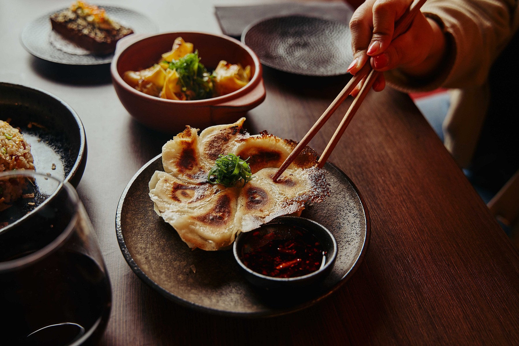 Chopsticks picking up dumplings at a restaurant table with side dishes — Melbourne food photography
