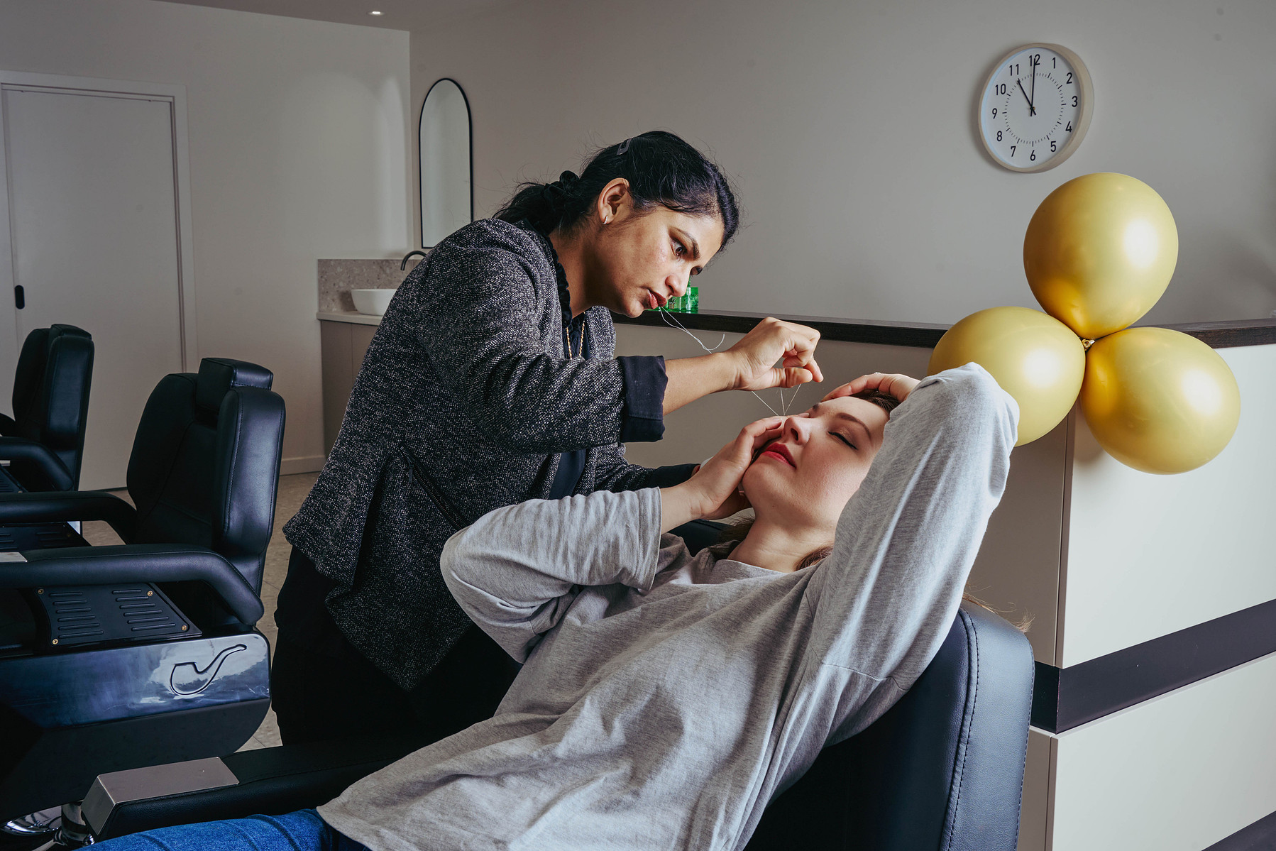eye brow specialist styling client’s brows in modern salon with gold balloons — Melbourne lifestyle and small business photography.