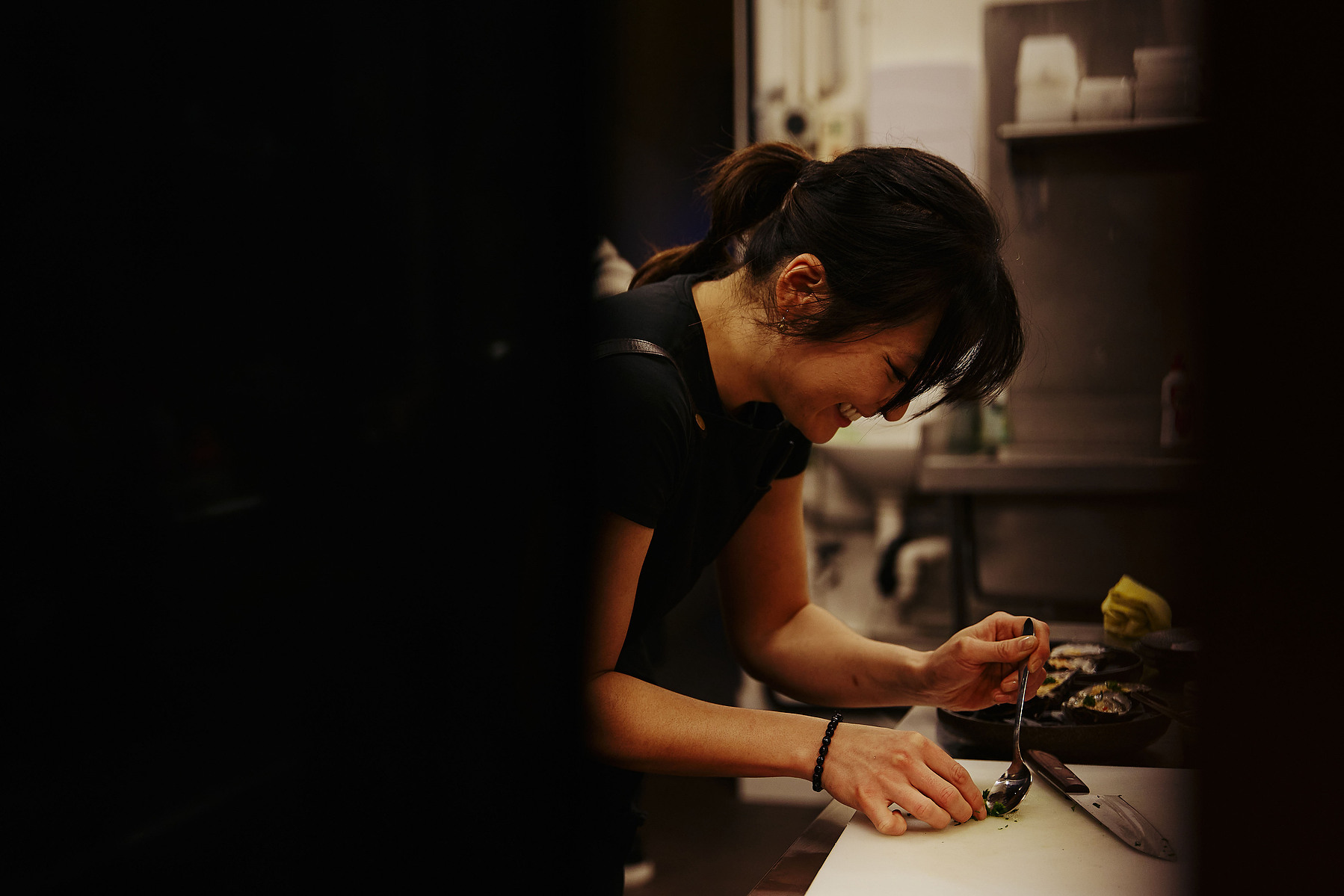  Female chef working in dimly lit kitchen plating food — Melbourne hospitality and chef portrait photography