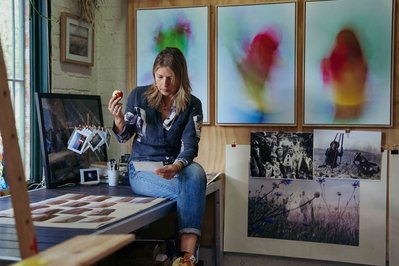 artist in her studio looking at photos and eating an apple