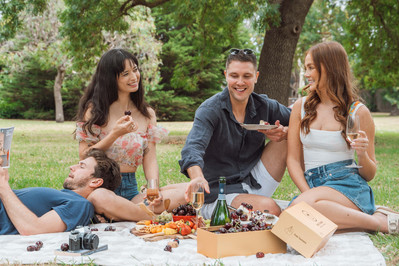 Group of friends sharing food and laughter at a Melbourne park picnic – shot by lifestyle photographer Marcie Raw