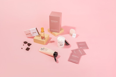 pink wellness products such as tea, hand cream, chocolate and a candle on a pink background 