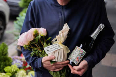 Close-up of person holding fresh flowers and a wrapped wine bottle at a Melbourne market