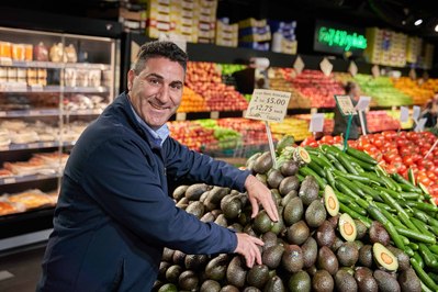 Man selecting avocados at a Melbourne fresh food market, smiling at the camera, captured by food photographer Marcie Raw