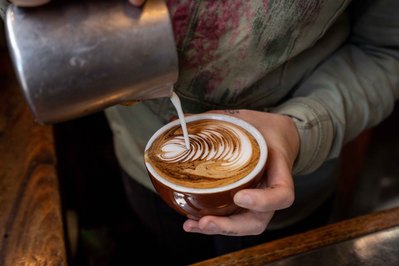 a close up shot of hands pouring milk onto the coffee cup