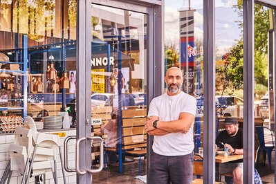 a cafe owner standing in front of his store and smiling at the camera
