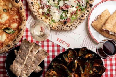 a spread of italian pizzas and wine on a checkered red and white tablecloth