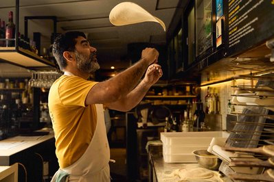 a pizza maker throwing a pizza dough in the air in a restaurant 