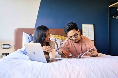 a couple of students lying on bed with a laptop and looking at the book together