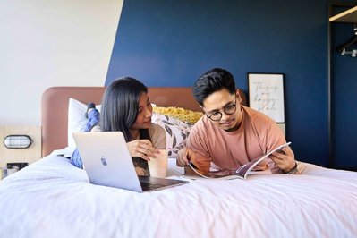 a couple of students lying on bed with a laptop and looking at the book together
