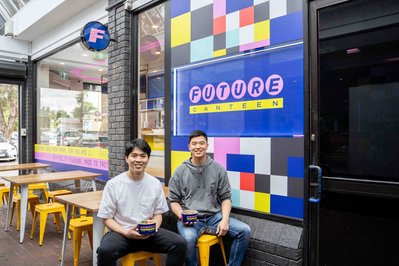 Japanese lunch place owners sitting on chair in front of their store and smiling at the camera