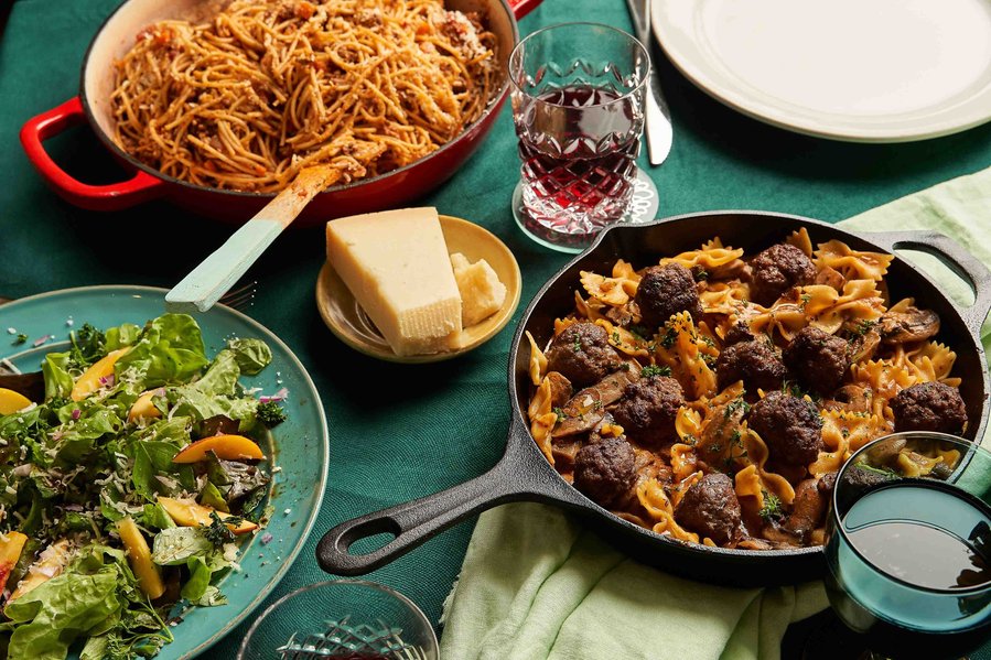 meatballs, pasta and a green salad spread on a dinner table
