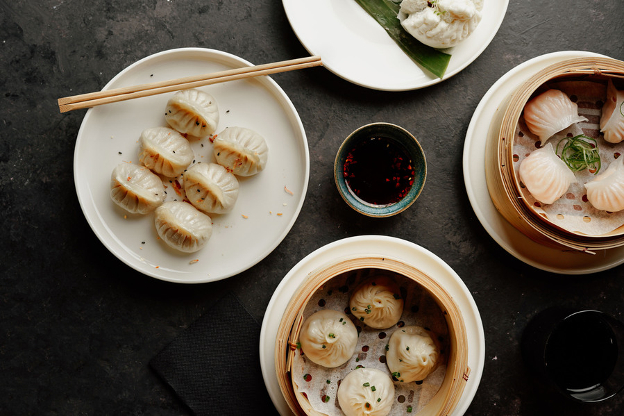 food spread of Chinese dumplings with chopsticks on a dark table