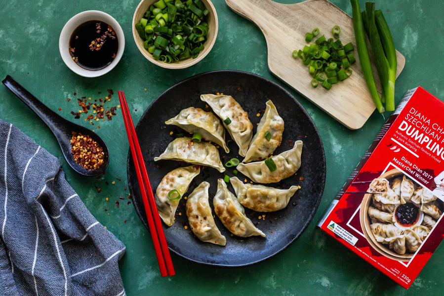 dumplings in the centre of the frame with small items such as chives, soy sauce, chilli lying around the plate