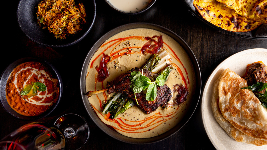 a food spread of chicken and Indian curries on a dark table