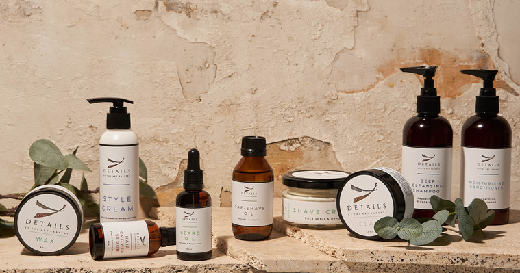 barber products such as beard oils and shampoos placed on a stone surface with eucalyptus leaves next to them