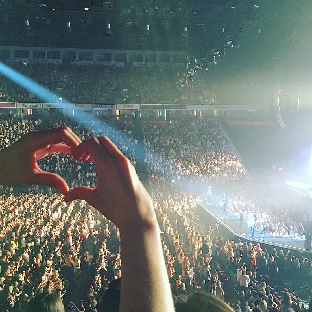 A girl makes a heart with her hands at a live concert at the Manchester AO Arena - Georgie Glass Photography