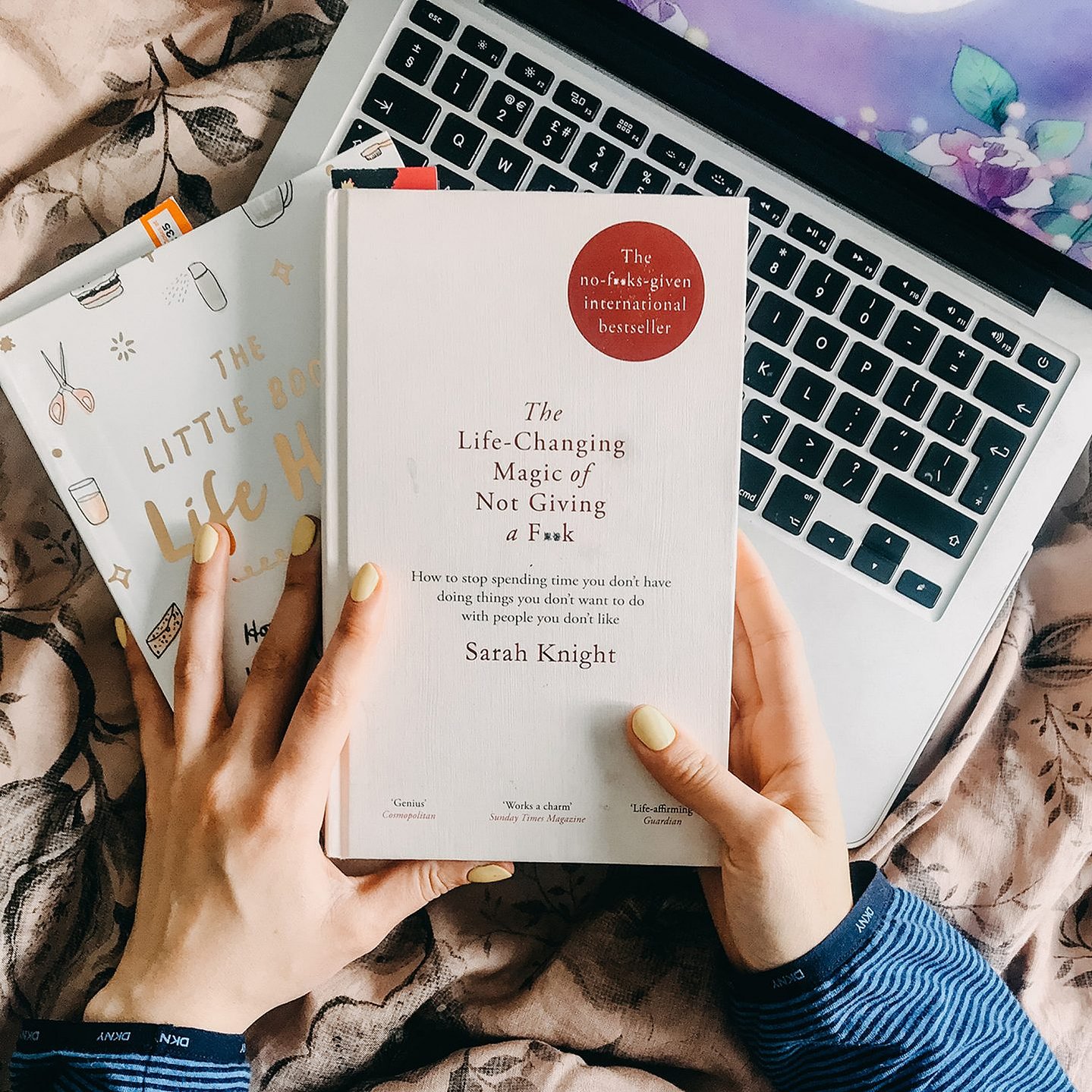 a girl sat in her pyjamas on the bed with her laptop reading 'The Life Changing Magic of not Giving a Fuck' by Sara Knight 