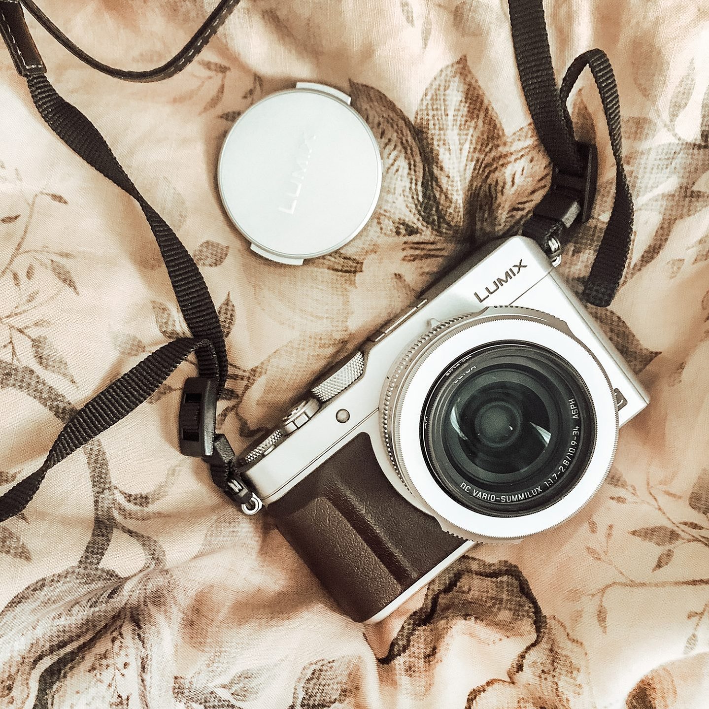 Lumix camera lies on a bed with floral bedding sheets, with the lens cap off