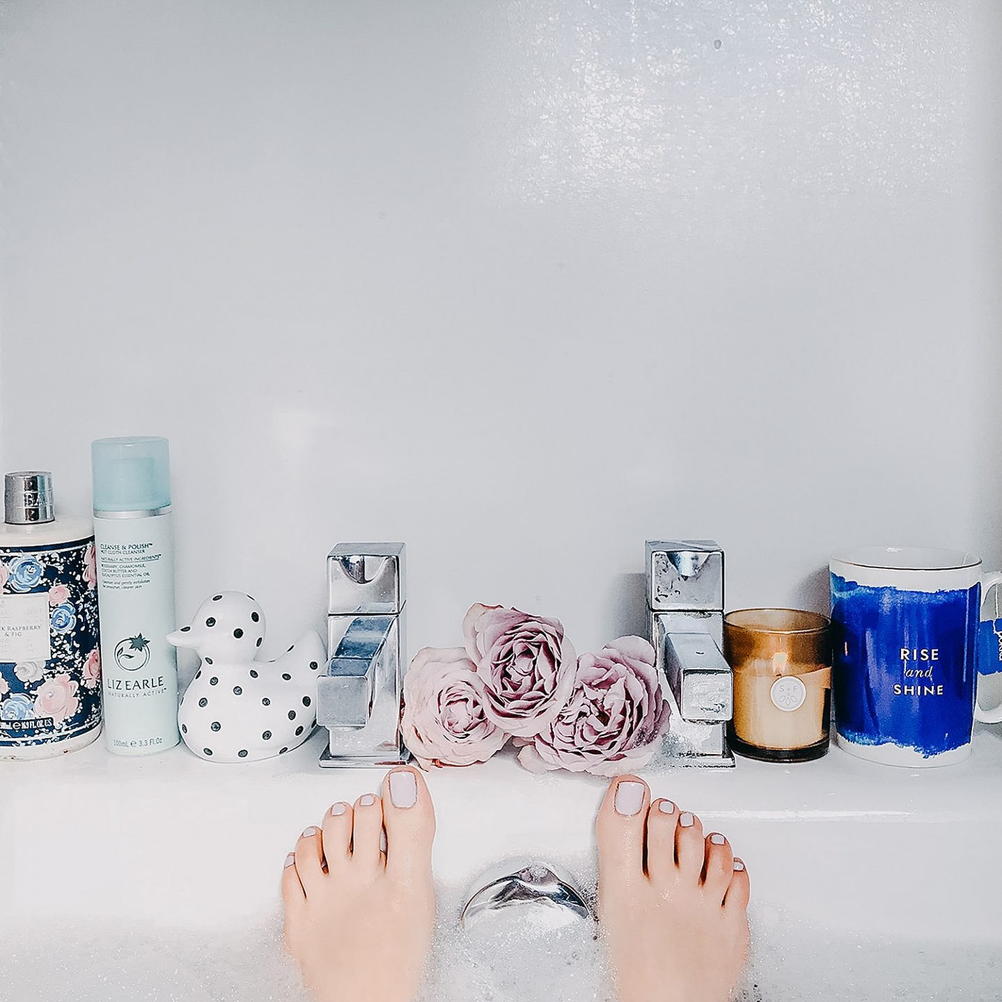 girl in a bubble bath with painted pink toes sticking out, with roses, bubble bath and ceramic ducks on the bath-side