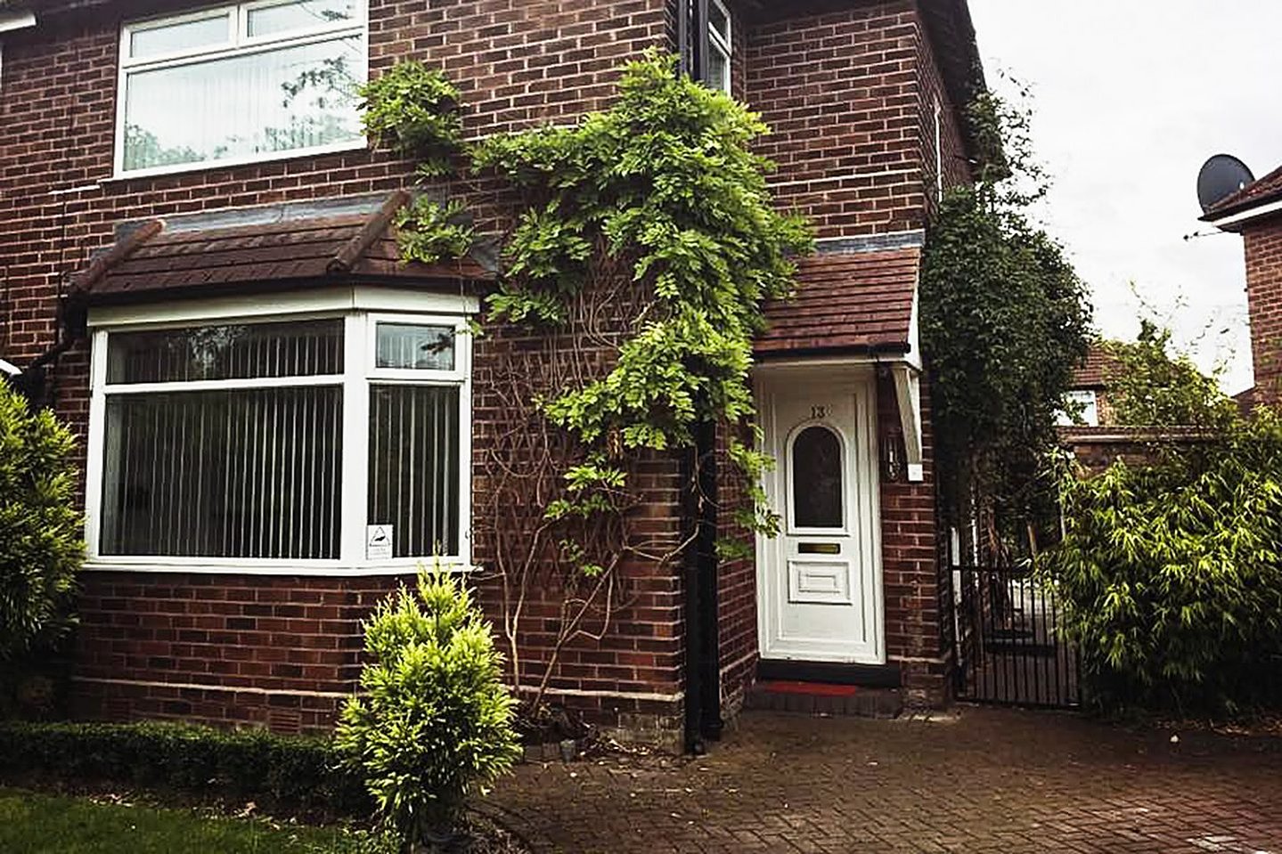 A front porch of a house, with foliage around the drain pipes and bay windows