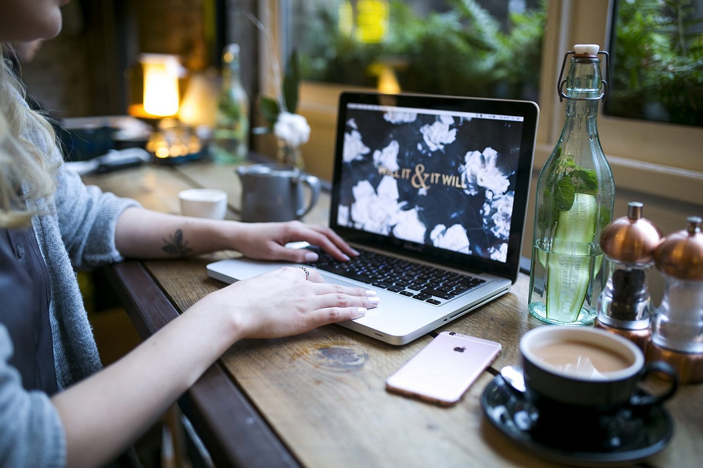 Girl types on a laptop in an atmospheric cafe environment surrounded by a latte,  her phone and other essentials