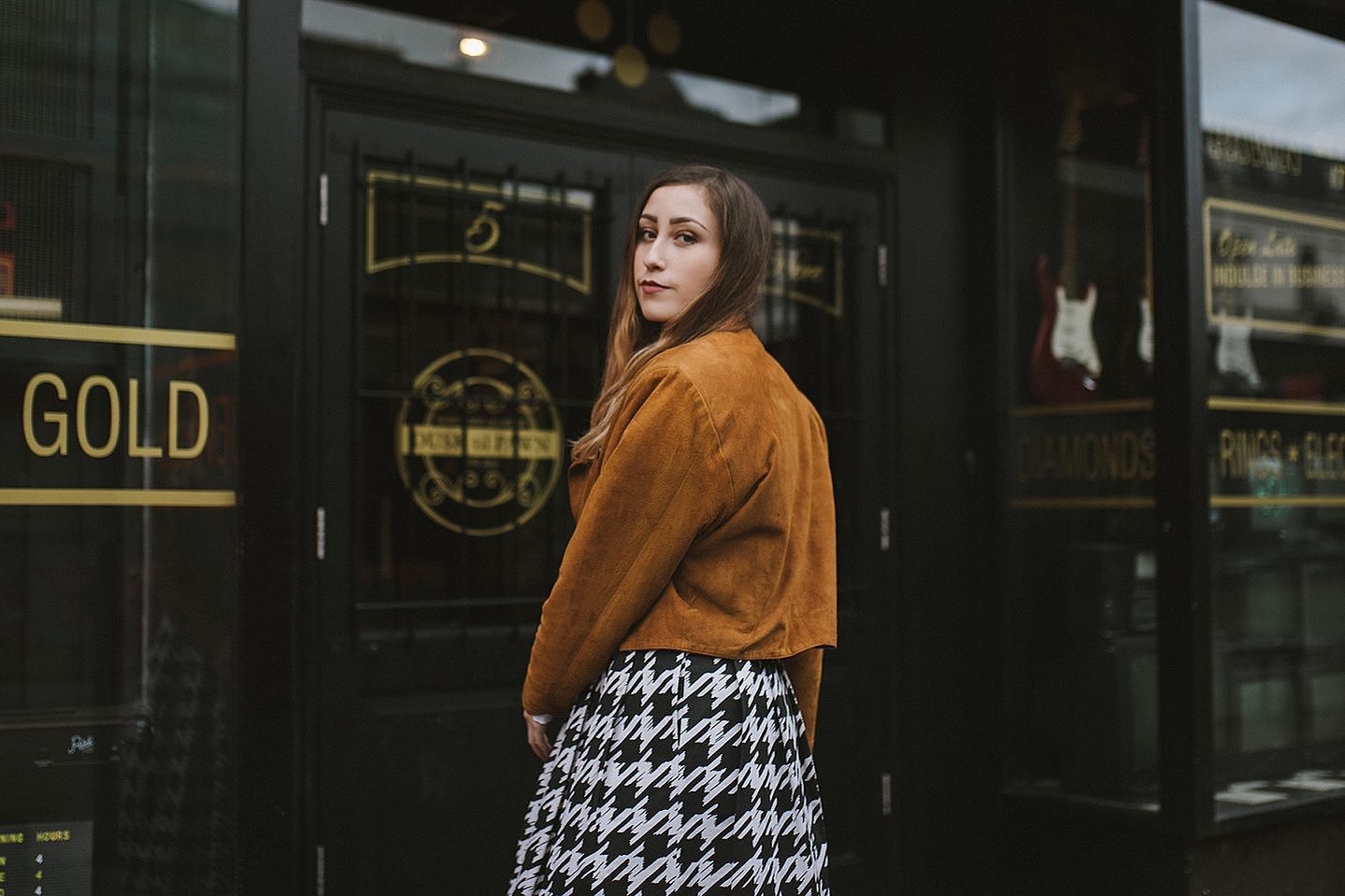 girl stands in Manchester city centres Northern Quarter, wearing a suede jacket and vintage skirt with brown hair