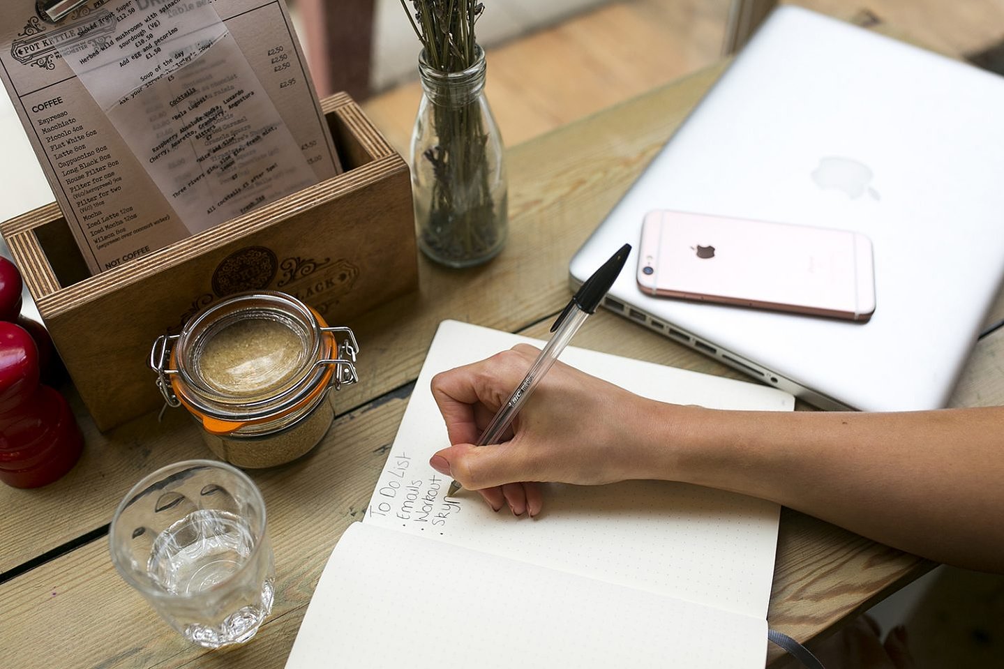 Girl writes in her notebook at a coffee shop,  surrounded by all her personal items - mobile phone, notepad, pen and latte