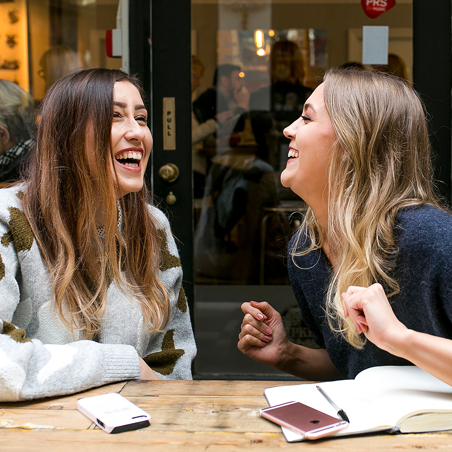 Georgie Glass Photography image of two women laughing at a desk with a notepad and mobile phones. Manchester photographer