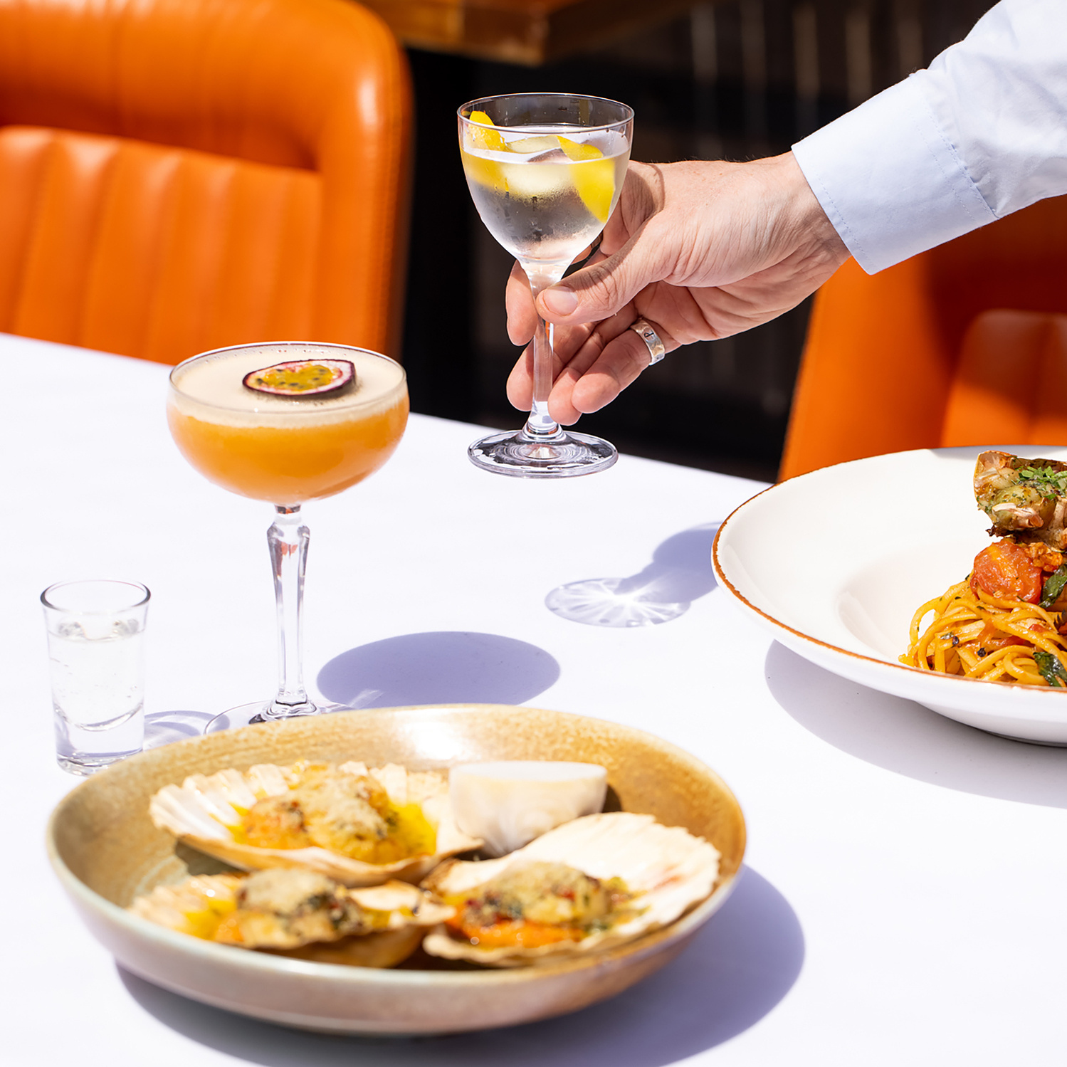 restaurant table set with food and two cocktails with hand reaching for one. Photography by Georgie Glass, Manchester